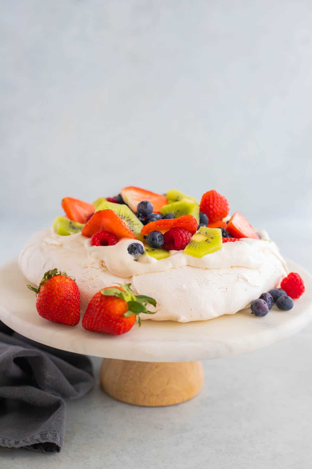 Pavlova topped with berries on a marble cake stand.