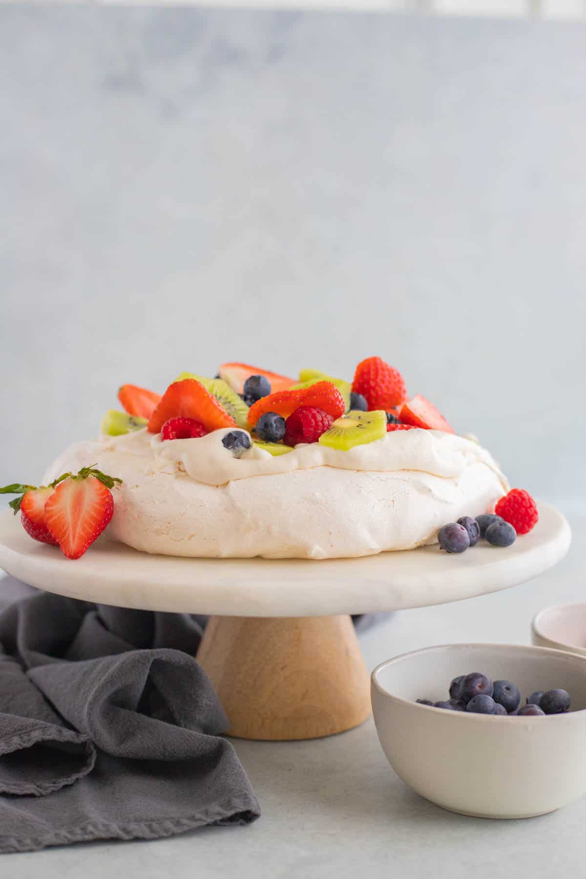 Pavlova topped with berries on a white cake stand.