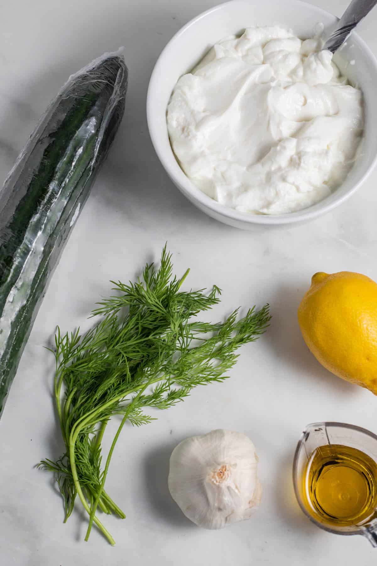 Ingredients for tzatziki laid on a marble surface.