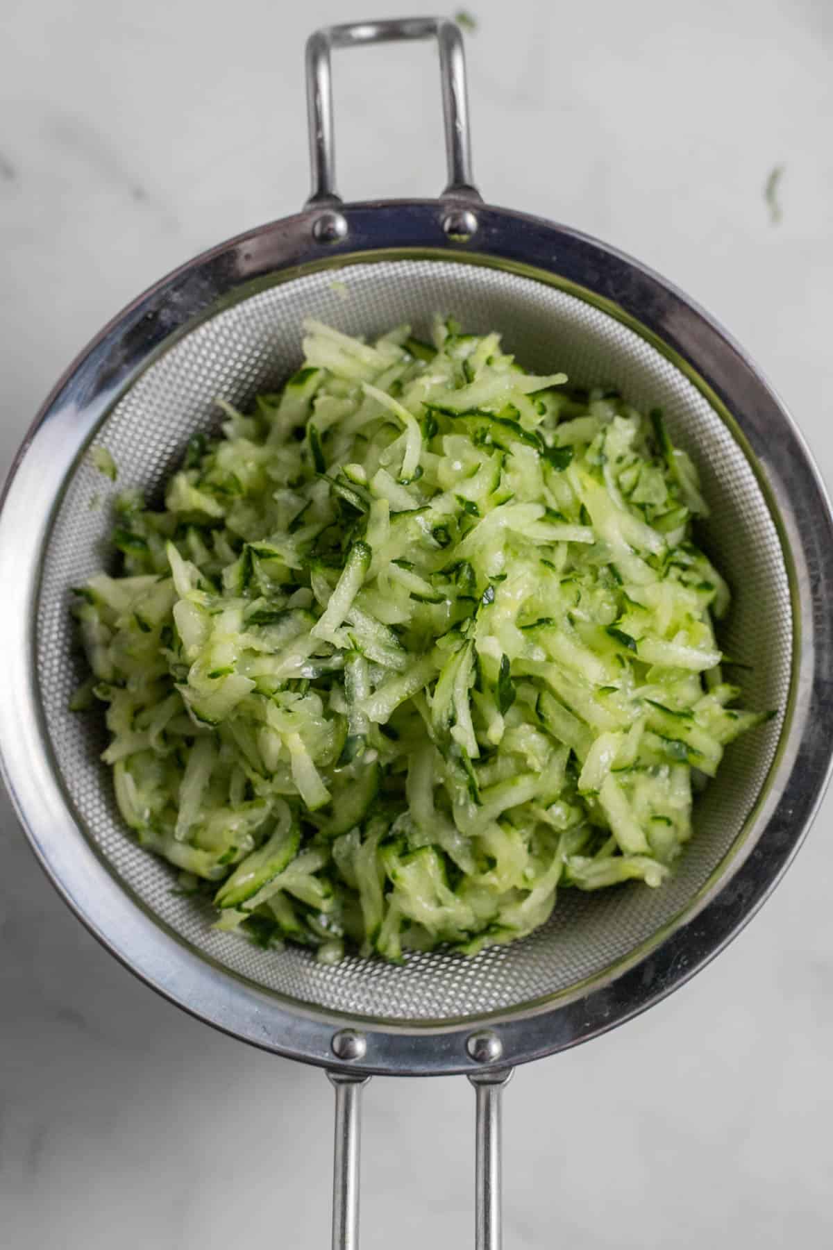 Shredded cucumber in a strainer.