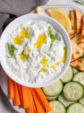 Greek tzatziki in a white bowl next to cucumbers and carrots.