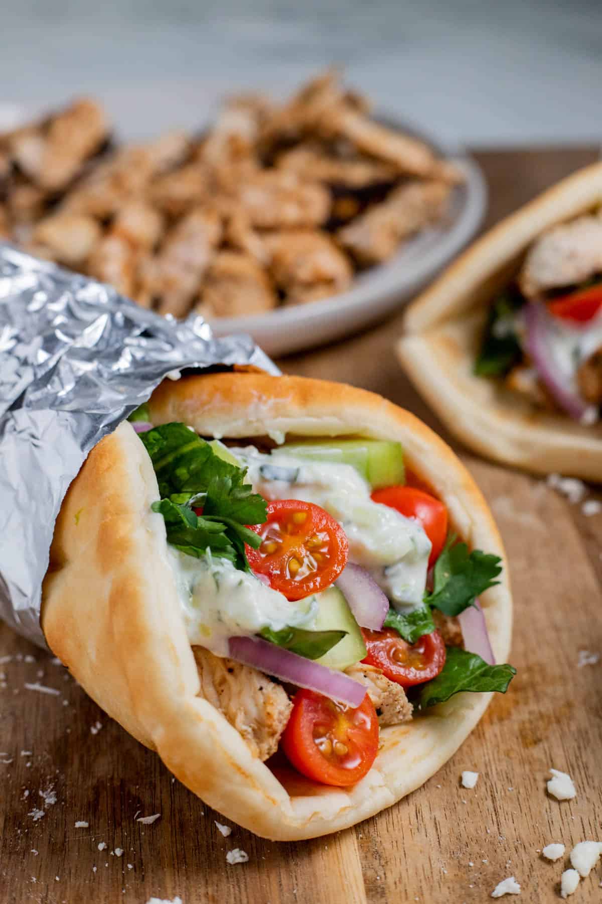 A Greek gyro wrapped in foil and placed on a wood surface.