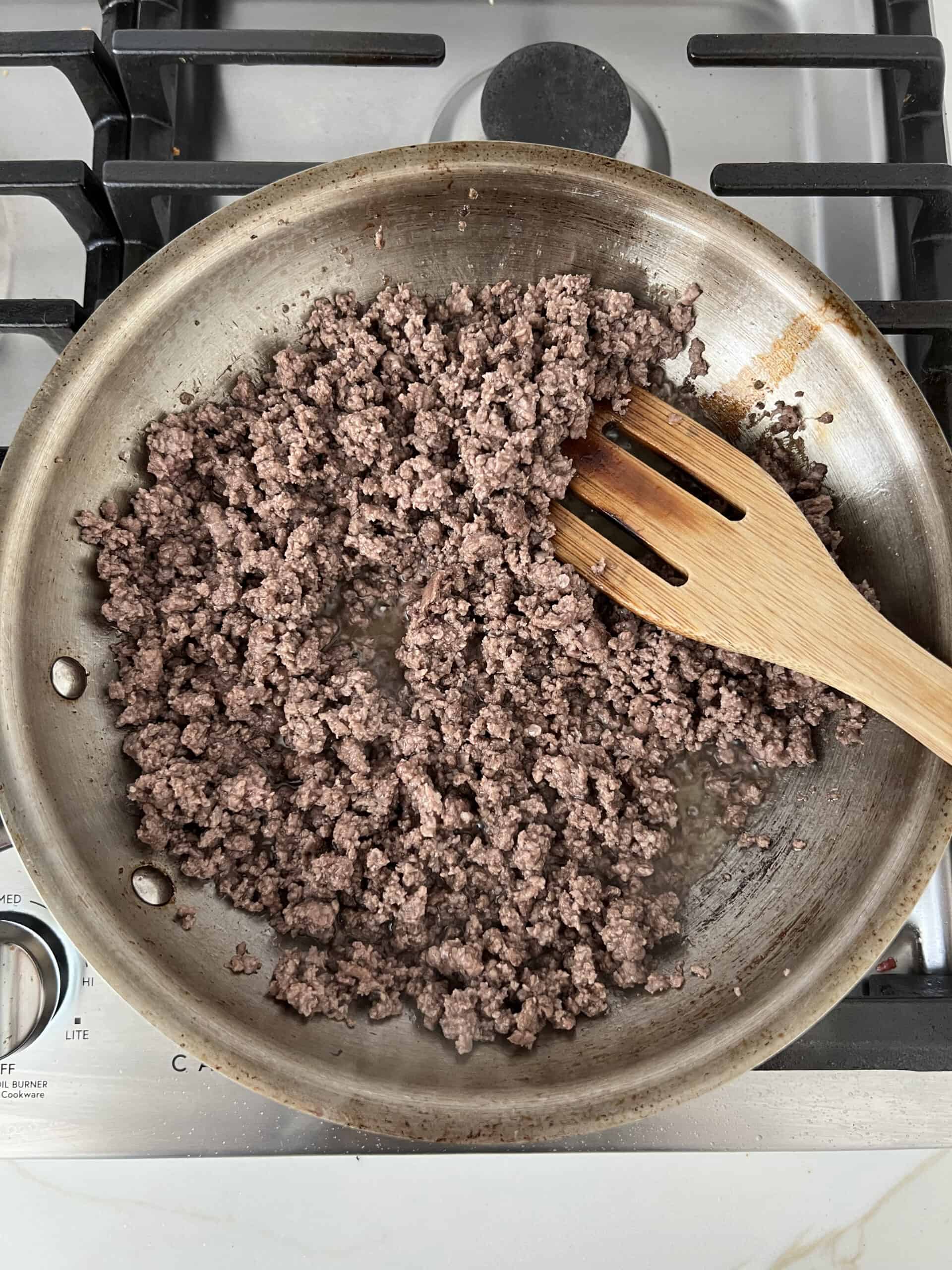 A frying pan with cooked ground beef in it.