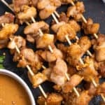 Cooked chicken satay on a black surface.