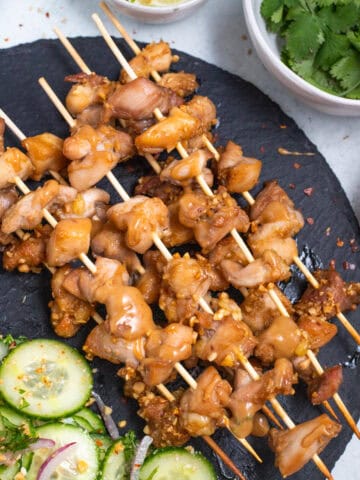 Chicken Satay on a black surface.