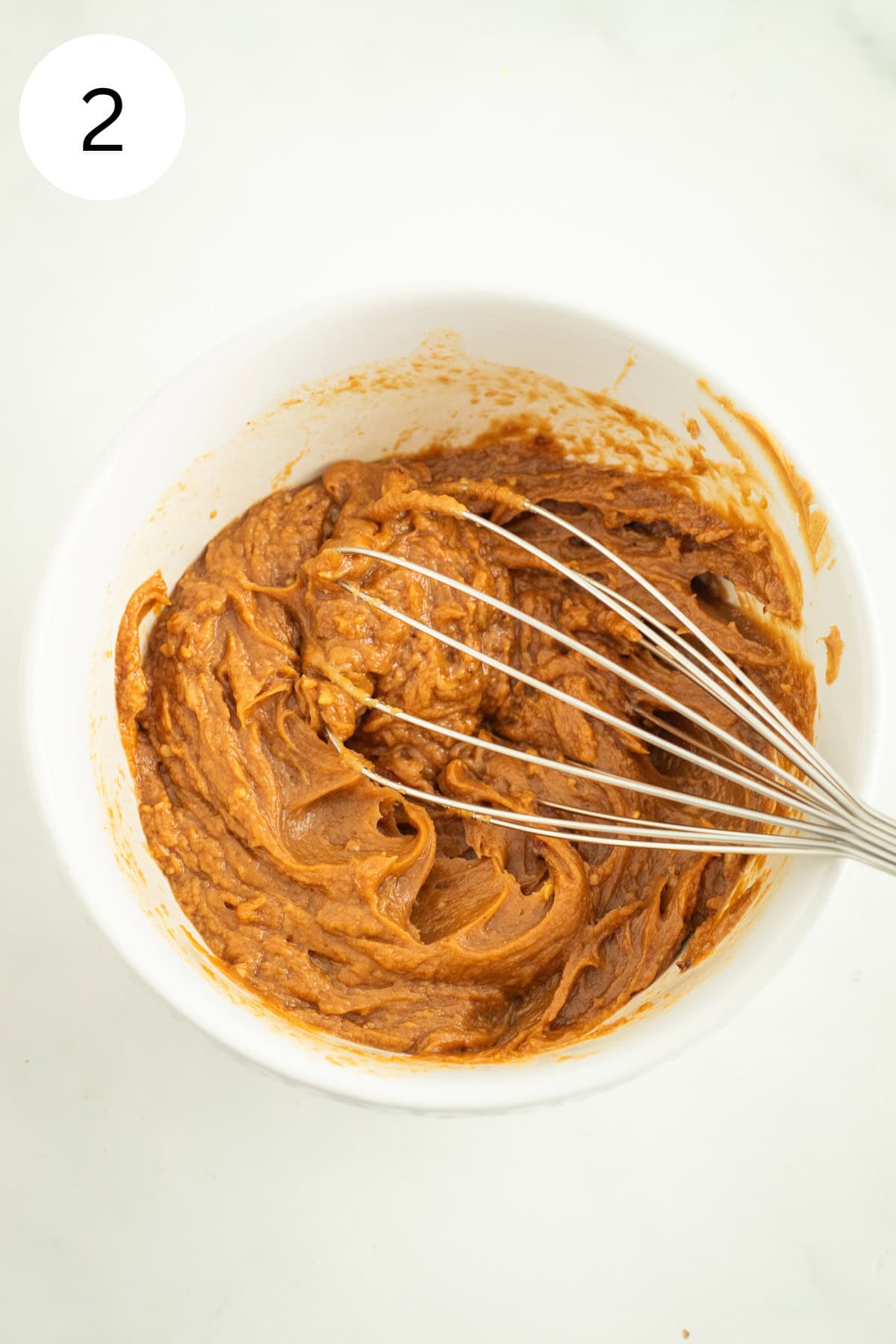 Peanut sauce in a white bowl with a whisk.