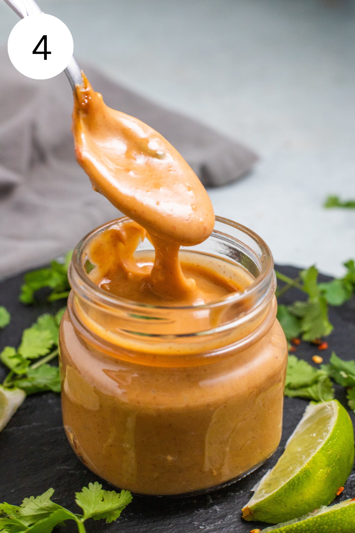 A spoon drizzling peanut sauce into a glass jar.