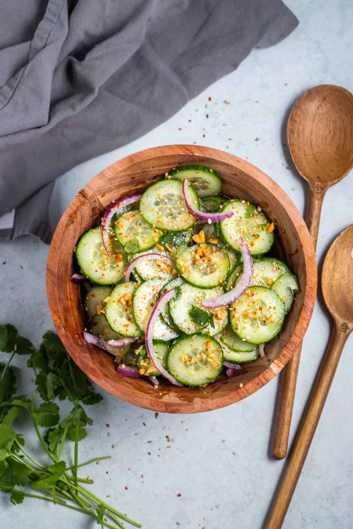 A top down view of thai cucumber salad in a wood bowl next to wooden salad spoons.