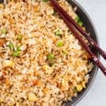 Egg fried rice in a gray bowl with chopsticks laid on the edge.