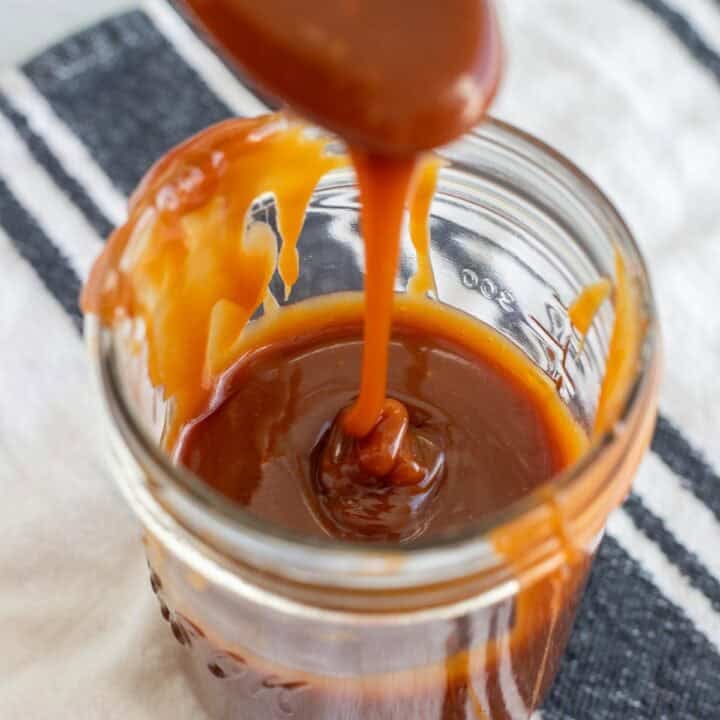 A spoon drizzling salted caramel sauce into a glass jar.