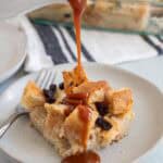 Drizzling salted caramel sauce on top of a piece of bread pudding. The pan with the rest of the pudding is in the background.