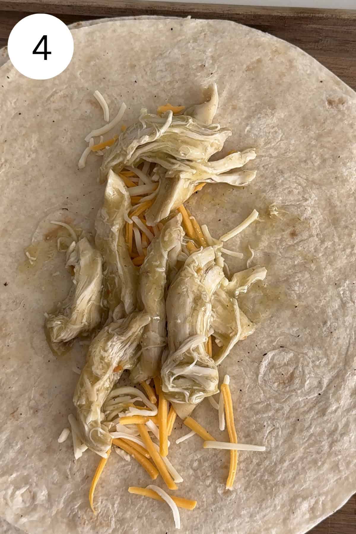 Flour tortilla topped with shredded chicken and shredded cheese.