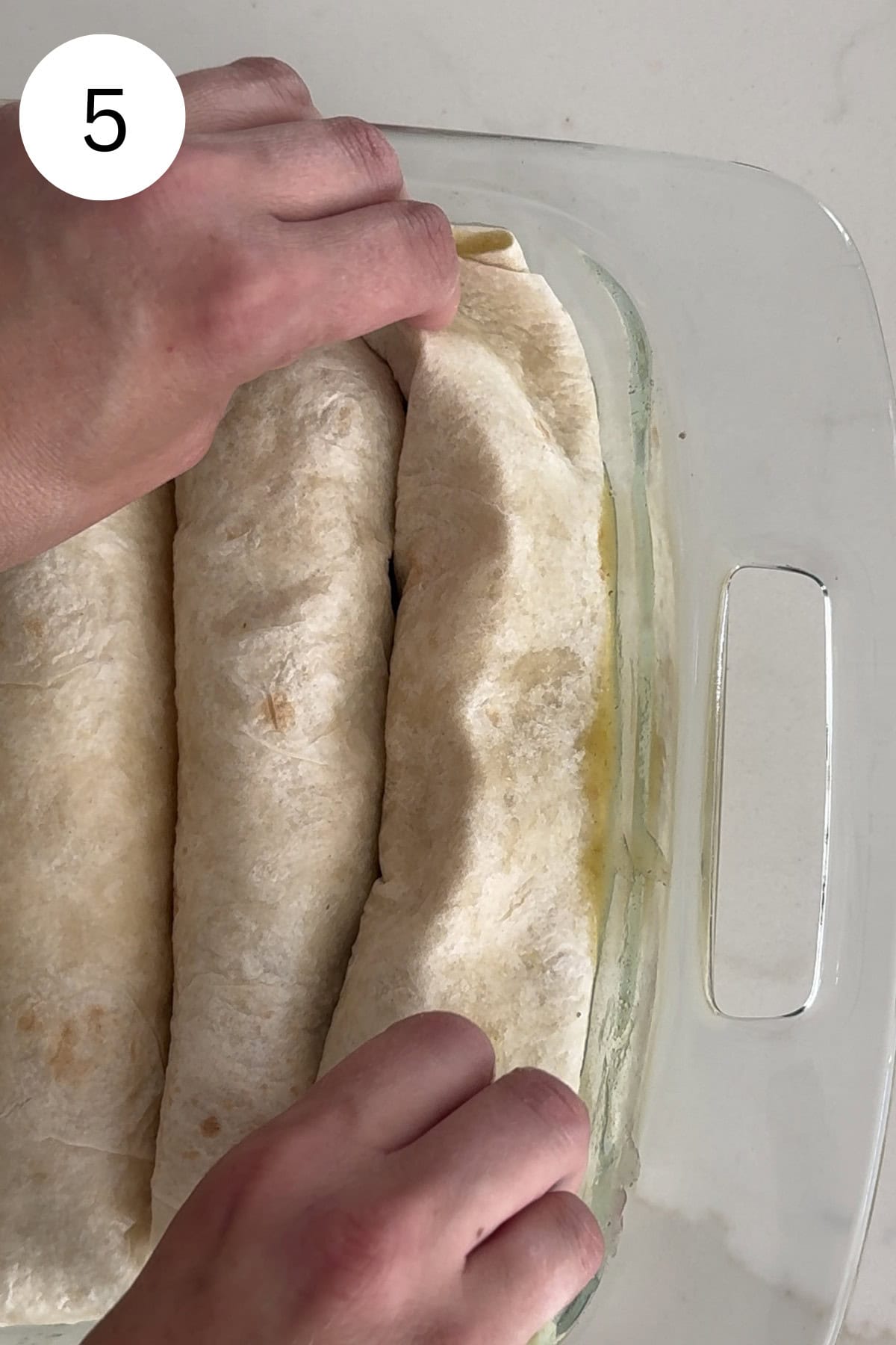 Hands placing enchilada into baking dish.