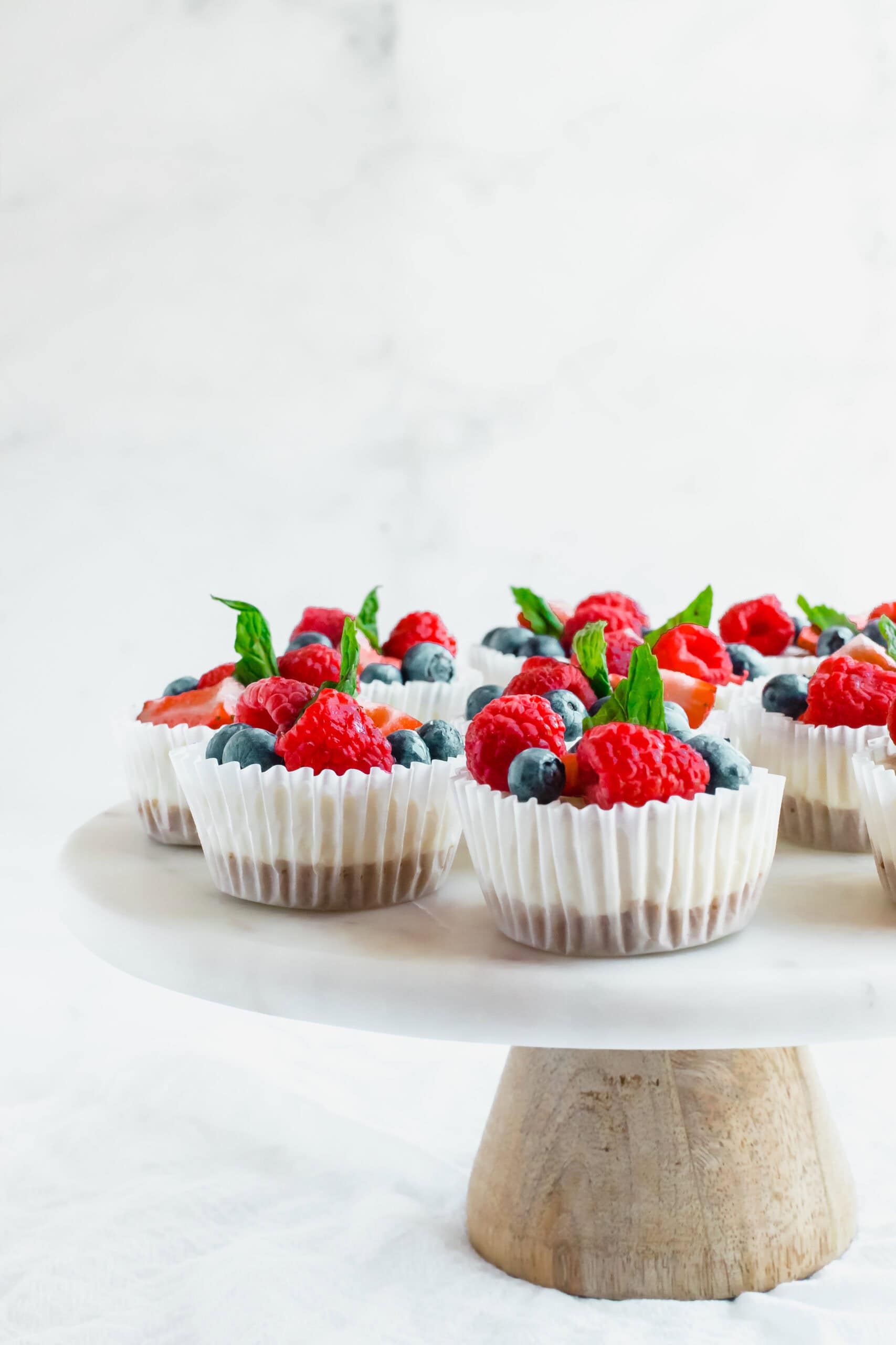 No-bake mini cheesecakes topped with fresh berries and placed on a cake stand.