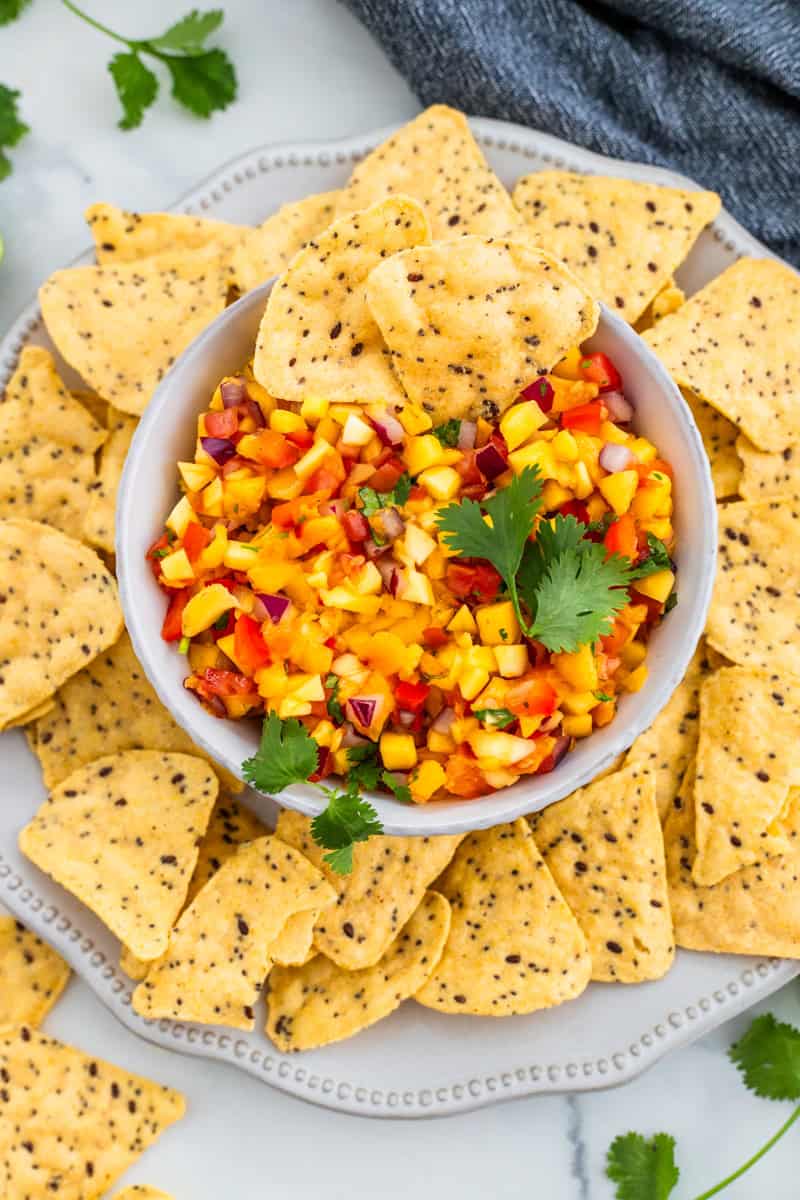A bowl of peach mango salsa with tortilla chips around it.