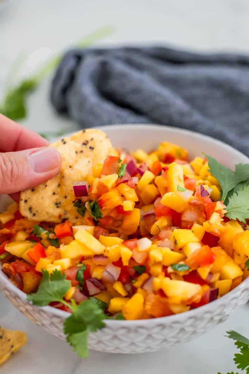 Hand dipping chip into bowl of peach mango salsa.