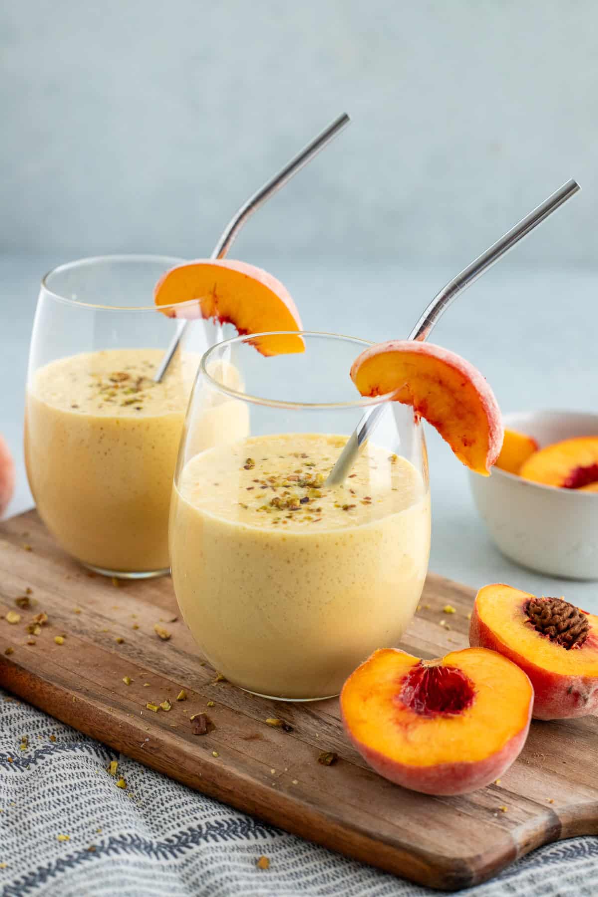 Two glasses of peach lassi garnished with metal straws and peach slices.