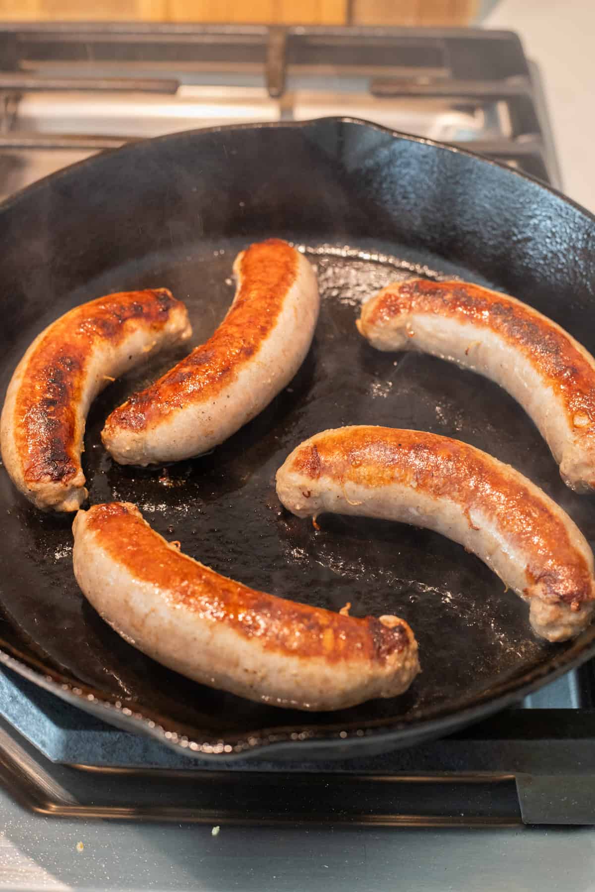 Brats browning in a cast iron skillet.