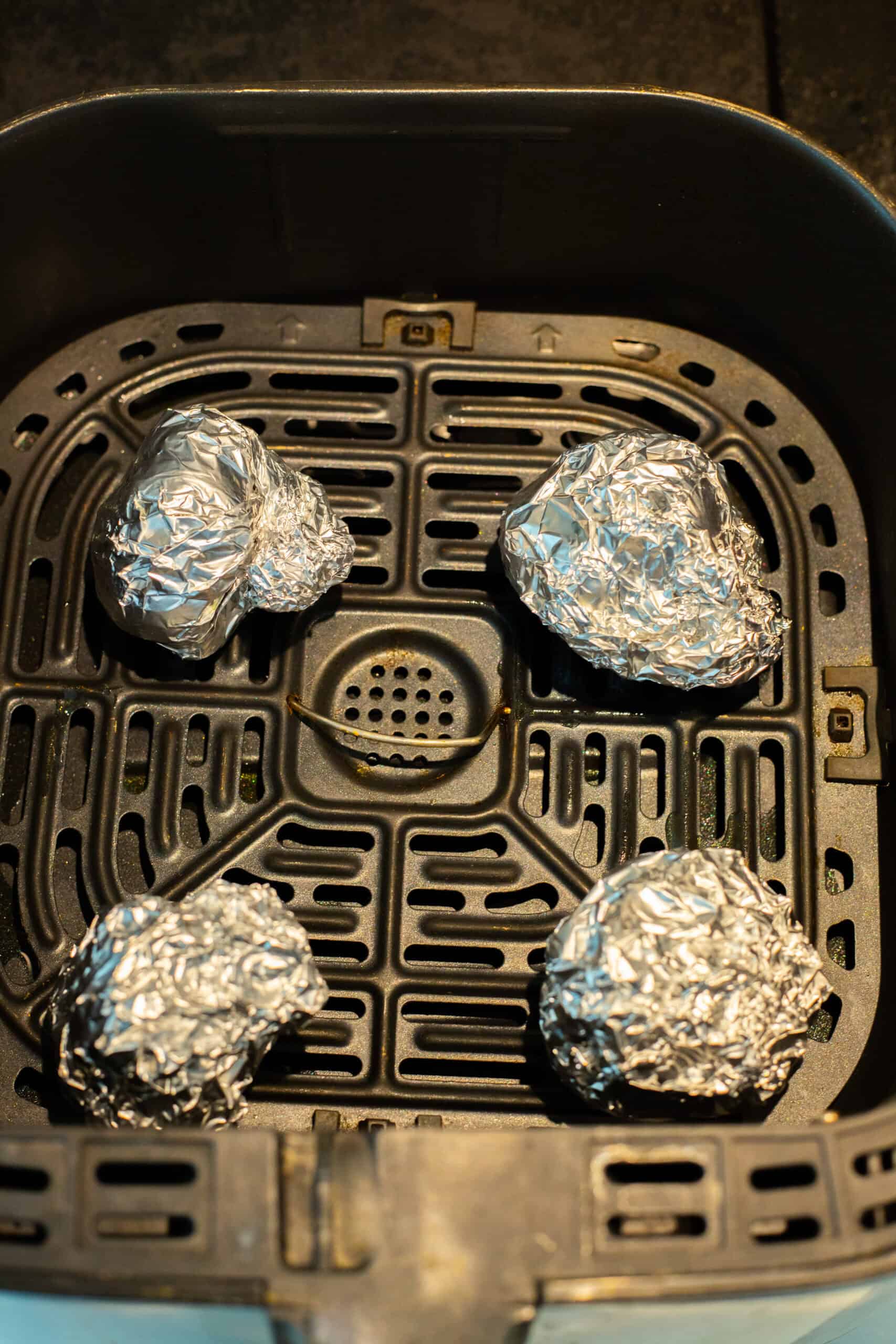 4 foil wrapped heads of garlic placed in an air fryer basket.