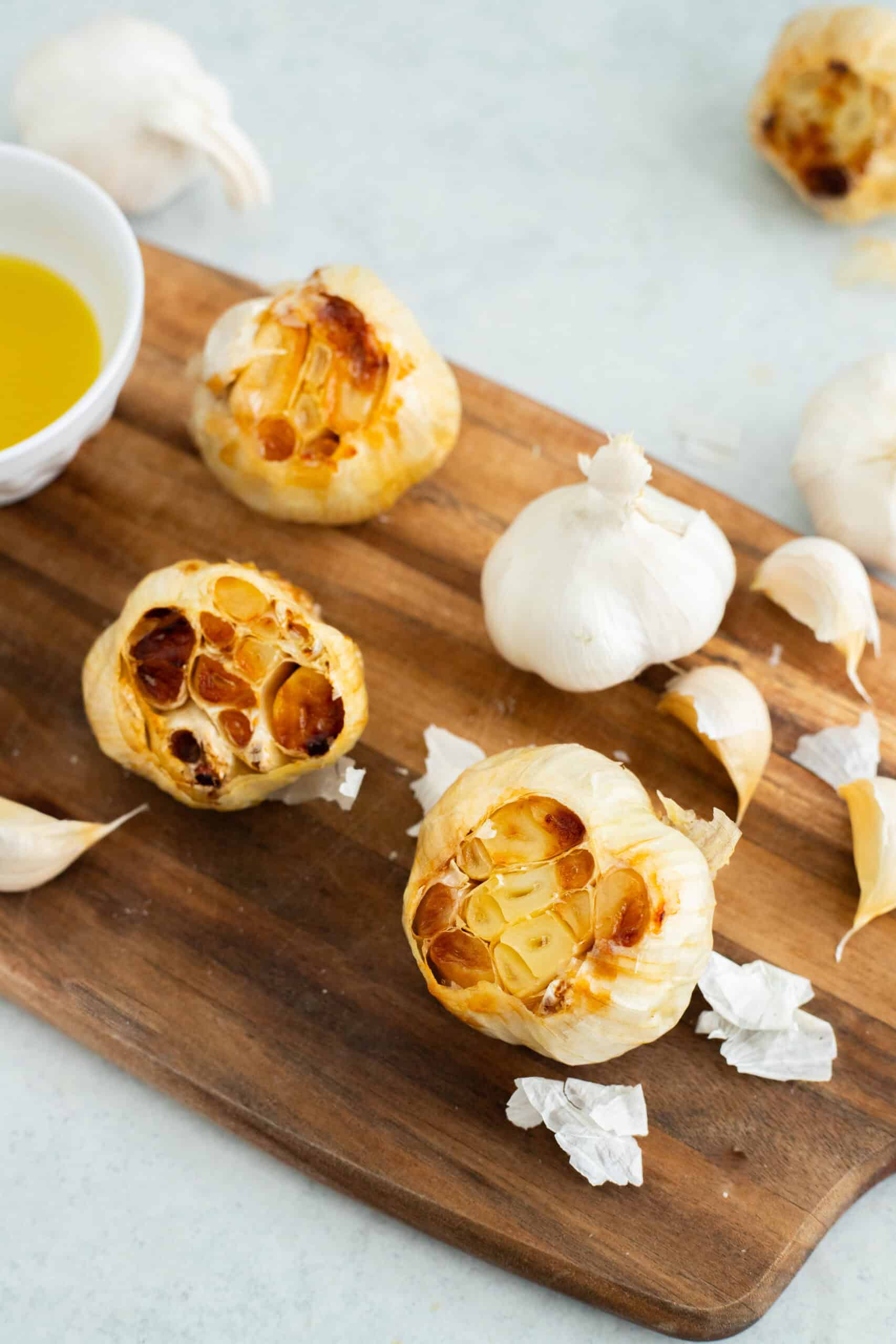 Roasted garlic heads on a wooden cutting board.