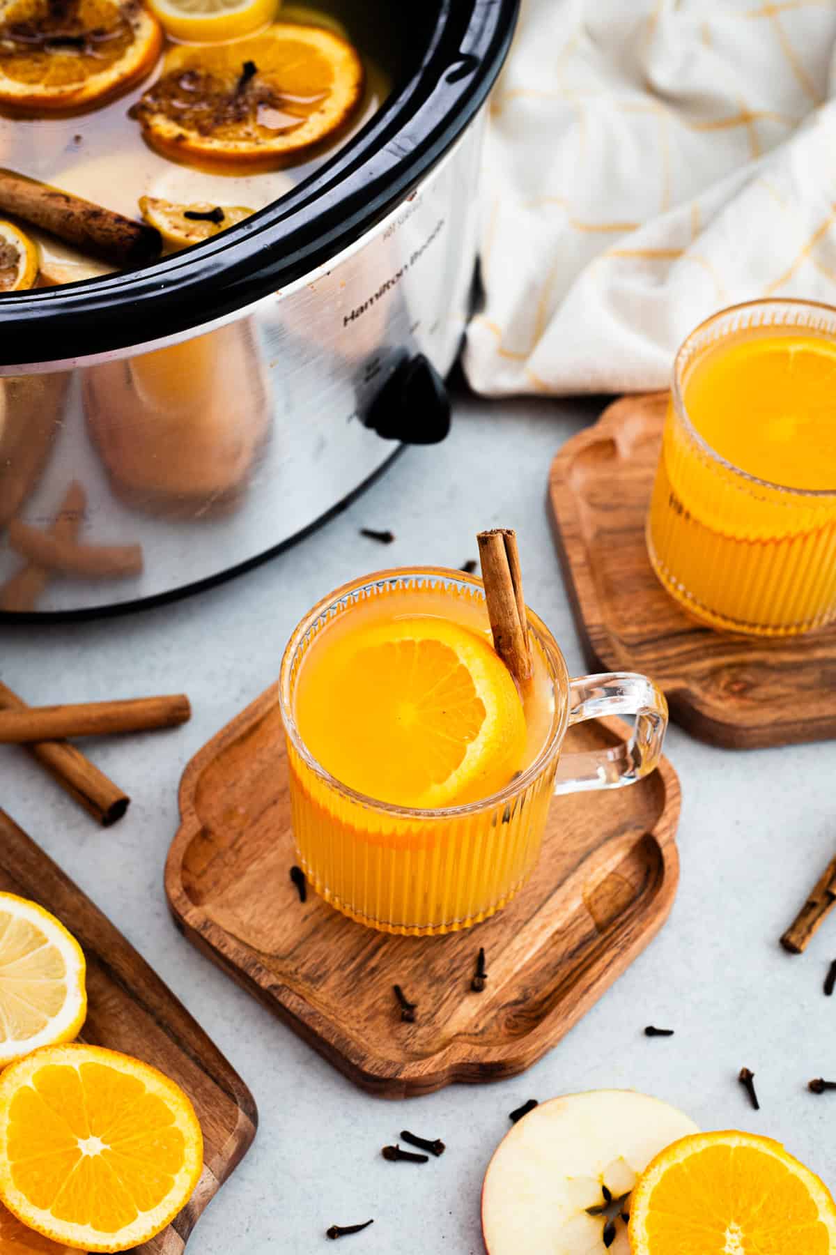 A glass mug of wassail garnished with orange slice and cinnamon stick.