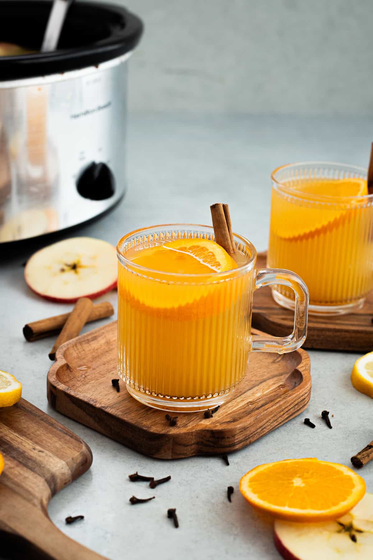 A glass mug of wassail garnished with an orange slice and cinnamon stick.