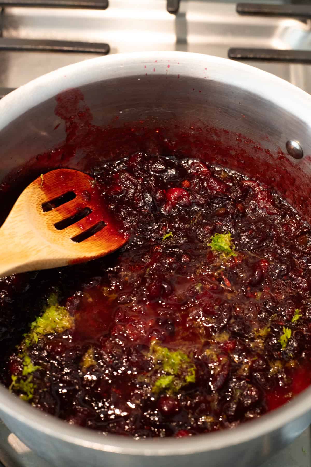 Stirring simmering cranberry sauce in saucepan.