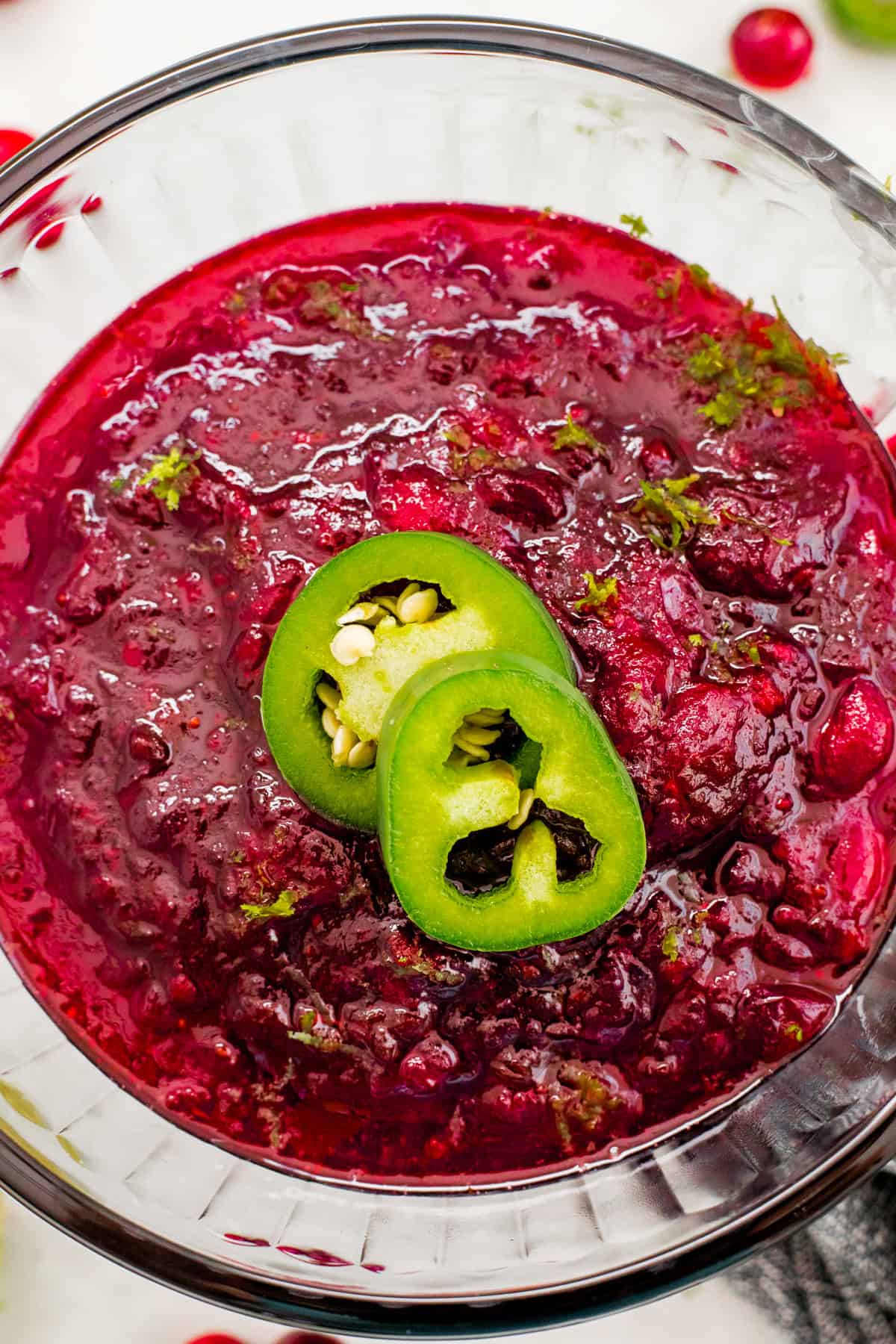 Cranberry sauce garnished with jalapeno slices in a glass bowl.